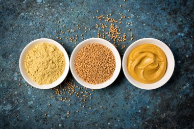 Geleneksel ev yapımı sos ve mavi beton arka planda baharatlı yemek için beyaz kâselere yerleştirilmiş hardal manzarası.