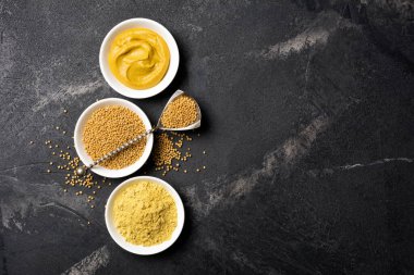 Geleneksel ev yapımı sos ve siyah mermer arka planda siyah kaşık ve fotokopi alanı olan baharatlı yemekler için beyaz kâselere yerleştirilmiş hardal manzarası.