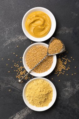 Geleneksel ev yapımı sos ve siyah mermer arka planda antika kaşıklı baharatlı yemekler için beyaz kâselere yerleştirilmiş hardal manzarası.