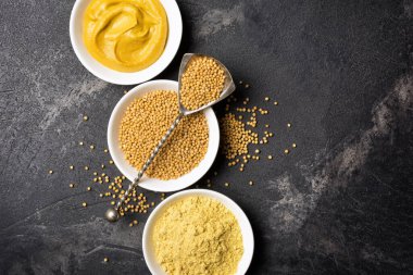 Geleneksel ev yapımı sos ve siyah mermer arka planda antika kaşıklı baharatlı yemekler için beyaz kâselere yerleştirilmiş hardal manzarası.