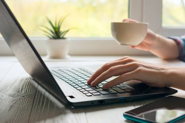 Bir fincan kahveyle eller. Siyah defter ve aydınlık pencere zemininde akıllı telefonları olan modern iş yeri