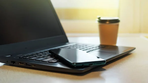 Modern work place at home for businesswoman or businessman with black notebook, smartphone and cup of coffee on light window background