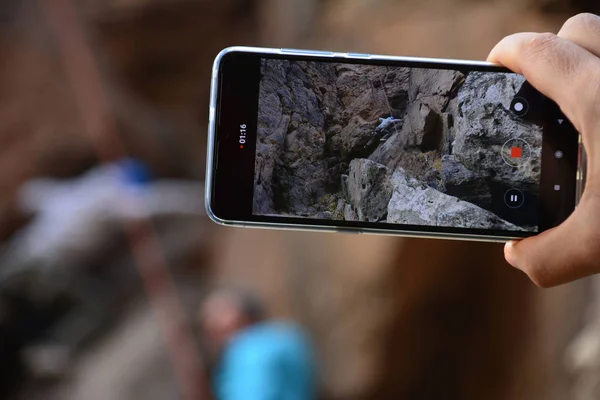 Bir dağın zirvesine tırmanmaya çalışan genç bir dağcı olarak akıllı telefondan fotoğraf çekiyor.