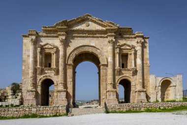 Jerash, Ürdün 'deki Romalı harabelerinde Hadrian kemeri. Mavi gökyüzü olan güneşli bir günde ön manzara. Sergide bazı alışılmadık, muhtemelen Nabataean, akanthus bazları gibi mimari özellikler yer alıyor..