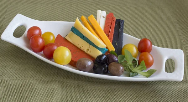 Platter of cheese in seven colors with olives and cherry tomatoes.