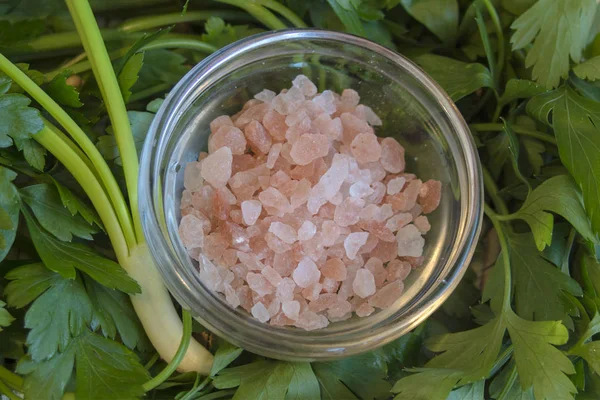 Himalayan crystal salt on a background of fresh parsley and a sprig of green onions.