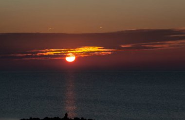 Denizin üzerinde gün doğumu. Güneşin yoluna karşı bir adamın silüetiyle.