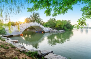 Pekin, Çin 'de yeşil bir bahçe göletinde eski tarz taş bir Çin kemer köprüsü.