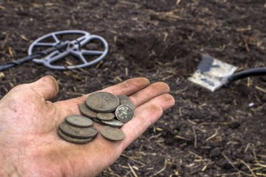 elinde bir metal dete alanıyla bulunan eski değerli paraları