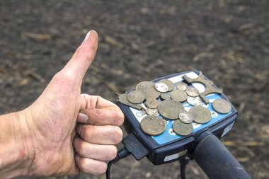 elinde bir metal dete alanıyla bulunan eski değerli paraları