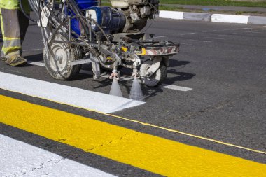 Yol işçileri şehrin asfalt yolundaki yaya geçidini boyamak için sıcak eritilmiş karalama makineleri kullanıyorlar..