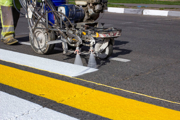 Road workers use hot-melt scribing machines to painting pedestrian crosswalk on asphalt road surface in the city.