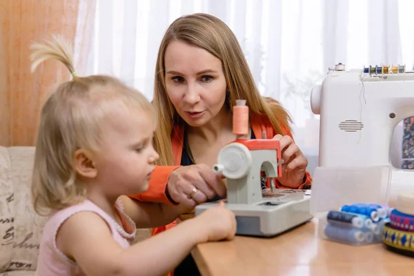 Mamá enseña a la pequeña hija a coser mientras juega —  Fotos de Stock