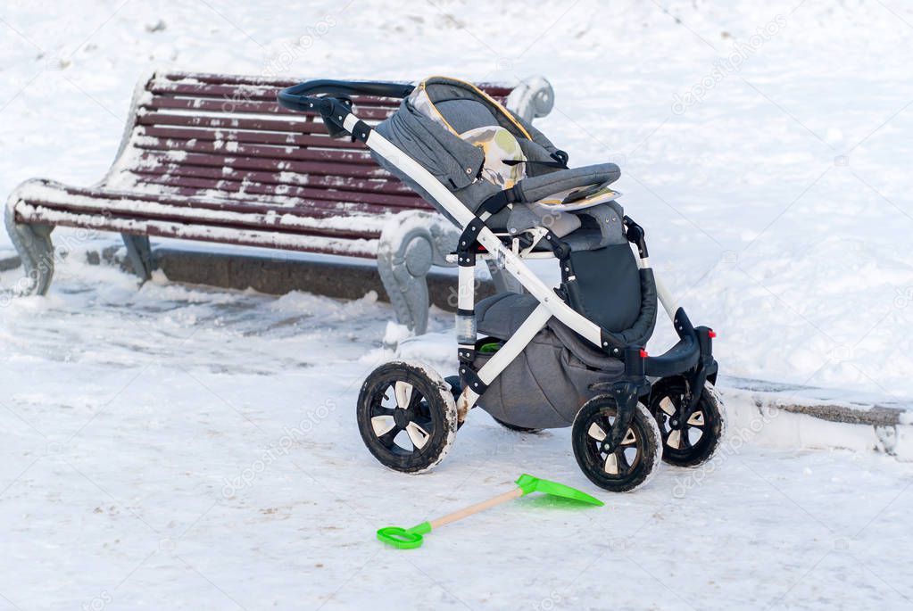 an empty baby stroller in the snow and a toy shovel near