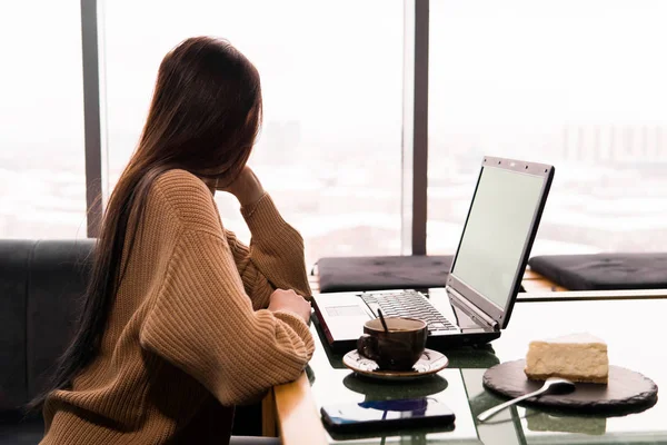 Giovane donna con un computer portatile in una caffetteria guarda con attenzione ou — Foto Stock