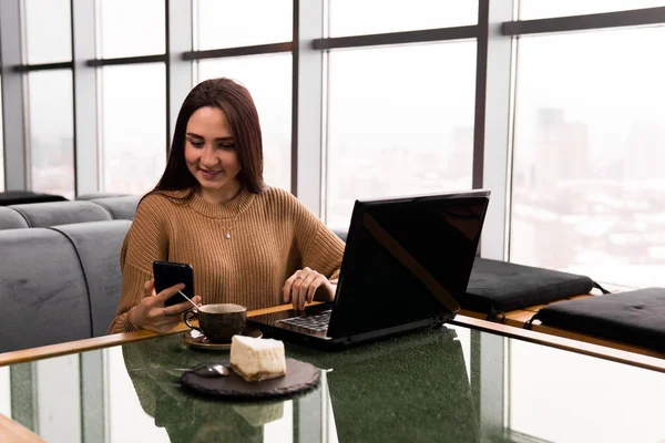 Молодая женщина работает с ноутбуком и смартфоном в кафе — стоковое фото