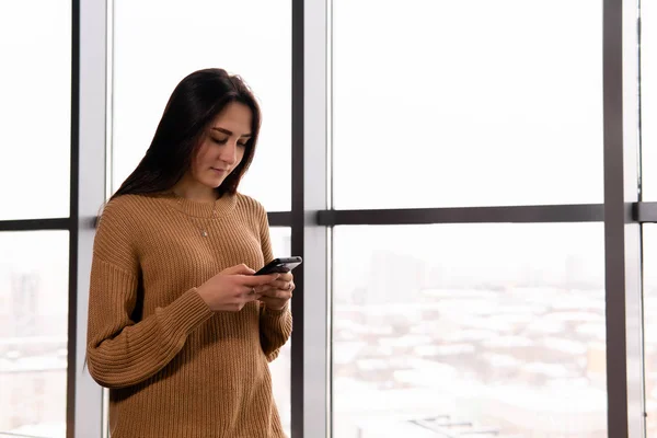 Mujer joven mira la pantalla de su teléfono contra la ventana — Foto de Stock