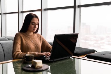 Bir kafede dizüstü bilgisayarda çalışan genç bir kadın.