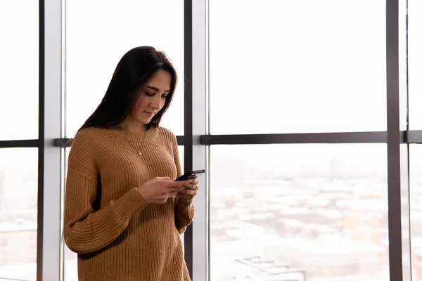 Mujer joven mira la pantalla de su teléfono contra la ventana — Foto de Stock