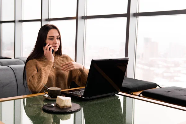 Молодая женщина работает на ноутбуке и разговаривает по телефону в кооперативе — стоковое фото