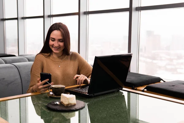 Mujer joven trabaja con el ordenador portátil y smartphone en una cafetería —  Fotos de Stock