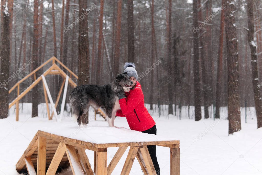 young woman hugs her dog in a winter dog park