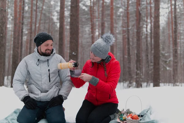 Mladý pár mají piknik ve sněžném lese, žena nalévá čaj — Stock fotografie