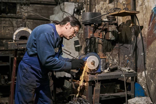 Handicraftsman processes a blacksmith's tool on a power grinding — Stockfoto