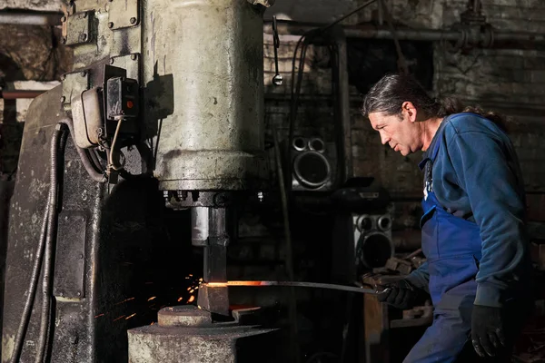 Blacksmith processes a hot workpiece with a machine hammer — 图库照片