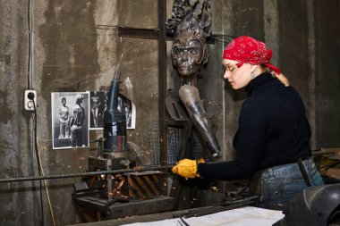 Perm, Russia - March 06, 2020: woman metal artist at work in workshop using metalcut saw