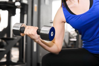 Spor salonunda bisepsler için halter egzersizi yapan bir kadının eli.