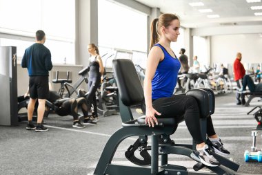 Perm, Russia - March 11, 2020: young petite woman performs reduction legs sitting on exercise machine in the gym