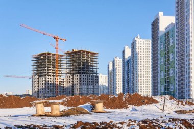 Çok katlı çok katlı apartmanların, inşaat halindeki binaların, tamamlanmış yüksek binaların ve ön planda boş kablolu makaraların olduğu bir caddenin inşasının manzarası