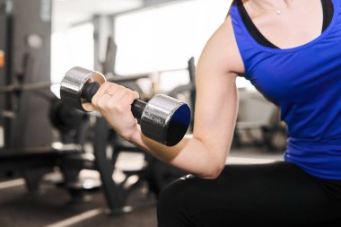 Spor salonunda bisepsler için halter egzersizi yapan bir kadının eli.