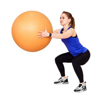 Genç bir kadın beyaz arka planda izole edilmiş fit topuyla çömelme hareketleri yaparak antrenman yapıyor.