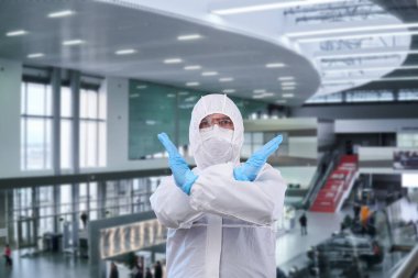 Tek kullanımlık anti-bakteriyel izolasyon giysisindeki adam epidemiyolojisti havaalanı ya da tren durağanlığına karşı yasaklama hareketi gösteriyor.