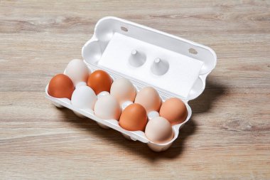 Beyazdan kahverengiye farklı tonlarda yumurtalar ahşap bir masa yüzeyinde tek bir yumurta sandığında bir araya getirilir.