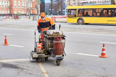 Perma, Rusya - 27 Nisan 2020: İşçi otobüs durağındaki asfaltı işaretlemek için yol işaretleme makinesi kullanıyor.