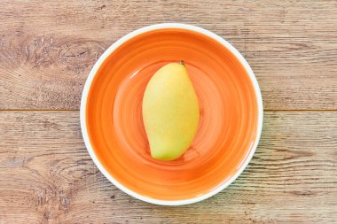 renk natürmort - soluk sarı mango meyvesi ahşap bir tabloda turuncu bir tabakta