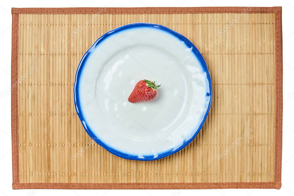 lonely berry of a strawberry on a white plate with a blue rim on a cane serving mat