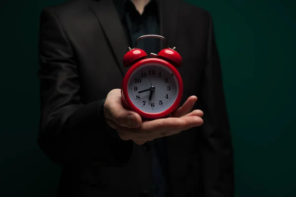 Homem em uma camisa escura e casaco detém um relógio vermelho — Fotografia de Stock