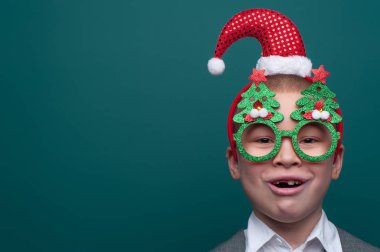 Noel Baba şapkalı küçük mutlu çocuk portresi ve Noel ağaçlı komik gözlükler.