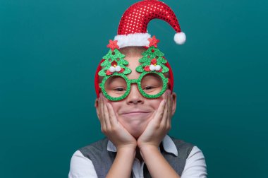 Noel Baba şapkalı küçük mutlu çocuk portresi ve Noel ağaçlı komik gözlükler.