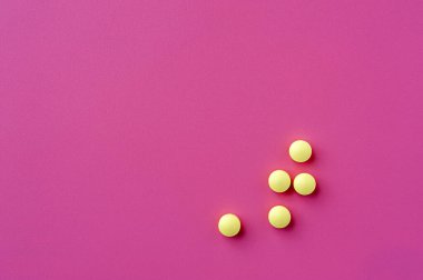 Close-up of yellow pills lie on a pink surface