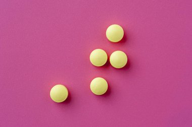 Close-up of yellow pills lie on a pink surface