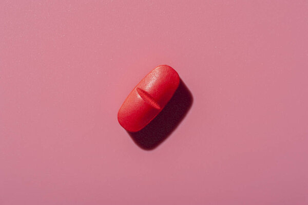 Close-up of one pill lies on a pink surface