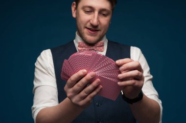 Elinde mavi arkaplanda poker kartları gösteren bir adam var.