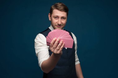 Elinde mavi arkaplanda poker kartları gösteren bir adam var.