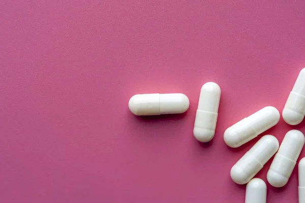 Close-up de pílulas brancas jazem em uma superfície rosa — Fotografia de Stock