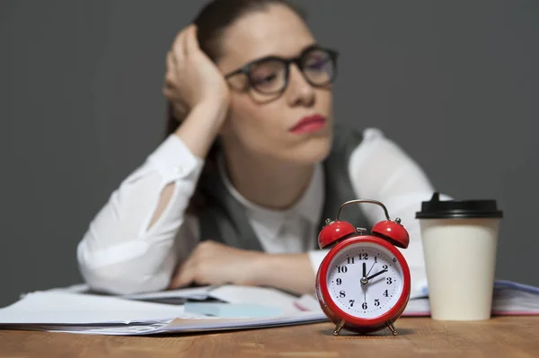 Fáradt irodai dolgozó az asztalnál papírokkal és piros ébresztőórával — Stock Fotó
